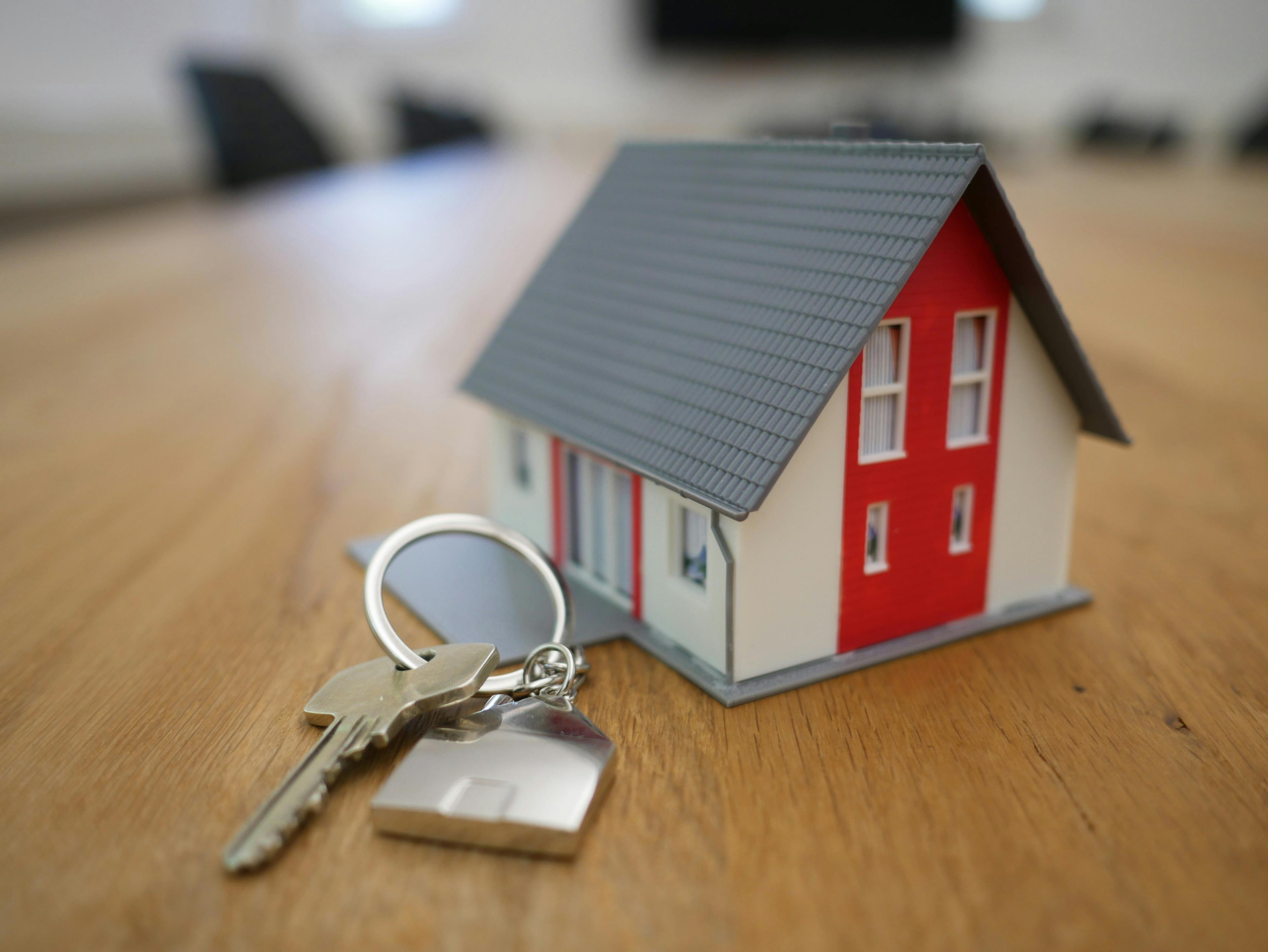 A tiny model red and white barn house on a table with a key to the right